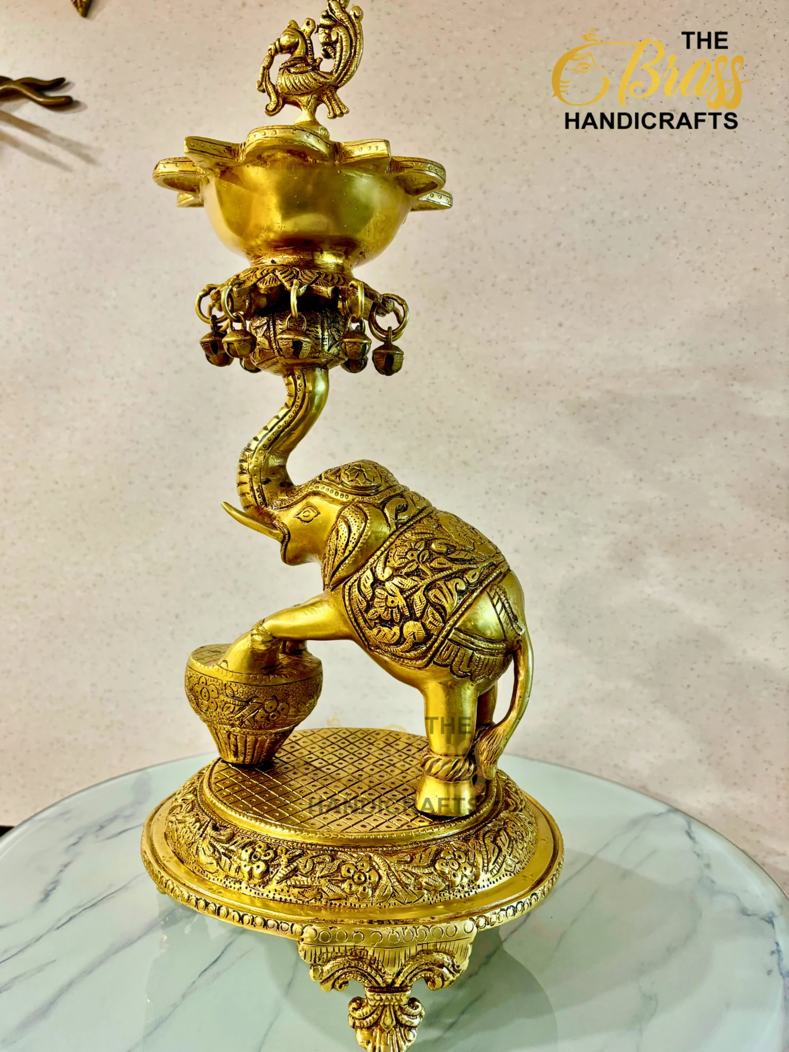 Ornate gold brass sculpture of a mythical creature with a curved neck and intricate patterns, displayed on a marble-topped glass table.  thebrasshandicrafts.com