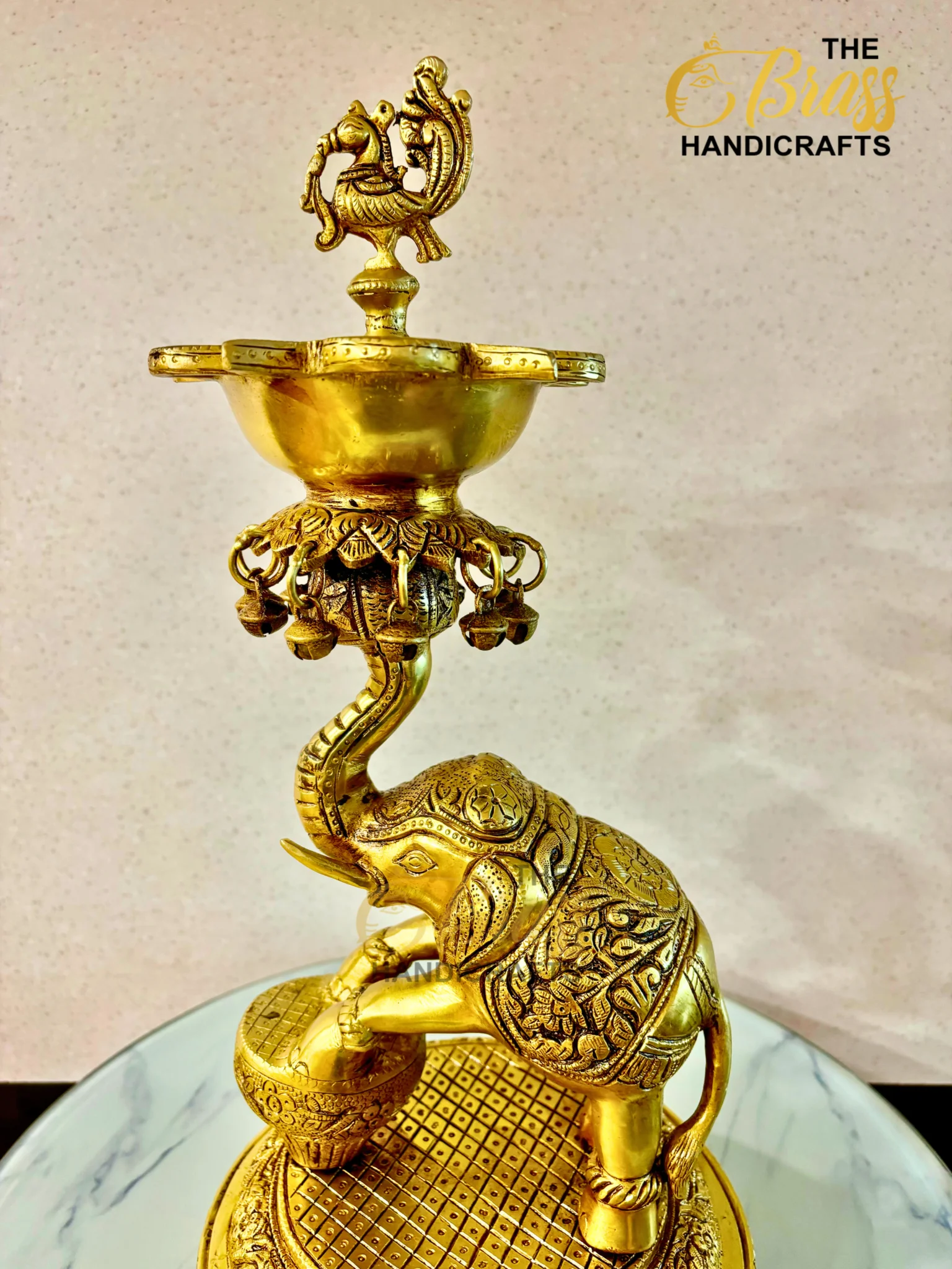 Ornate gold brass lamp with a sculpted bird finial on top and hanging decorative bells beneath.  thebrasshandicrafts.com