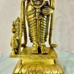 Close-up of a gold brass statue's lower torso, hands, and ornate belt, standing on a carved pedestal with decorative patterns; watermark 'The Brass Handicrafts' visible in the corner.  thebrasshandicrafts.com