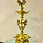 Ornate brass hookah with a peacock finial stands on a marble-topped table, logo 'The Brass Handicrafts' in the corner.  thebrasshandicrafts.com