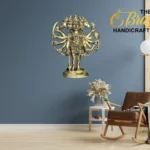 Ornate brass multi-armed deity statue mounted on a blue wall, with 'The Brass Handicrafts' logo in the corner and a rocking chair nearby.  thebrasshandicrafts.com