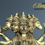 Gold-toned brass statue of a multi-headed Hindu deity with many arms, set against a blue background; The Brass Handicrafts logo in the top-right corner.  thebrasshandicrafts.com