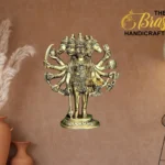Brass multi-armed Hindu deity statue displayed in a home decor setting with a warm brown wall and The Brass Handicrafts logo in the corner.  thebrasshandicrafts.com