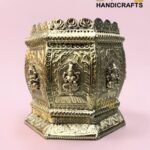Gold ornate brass shrine with Buddha reliefs and intricate patterns on a pink background.  thebrasshandicrafts.com