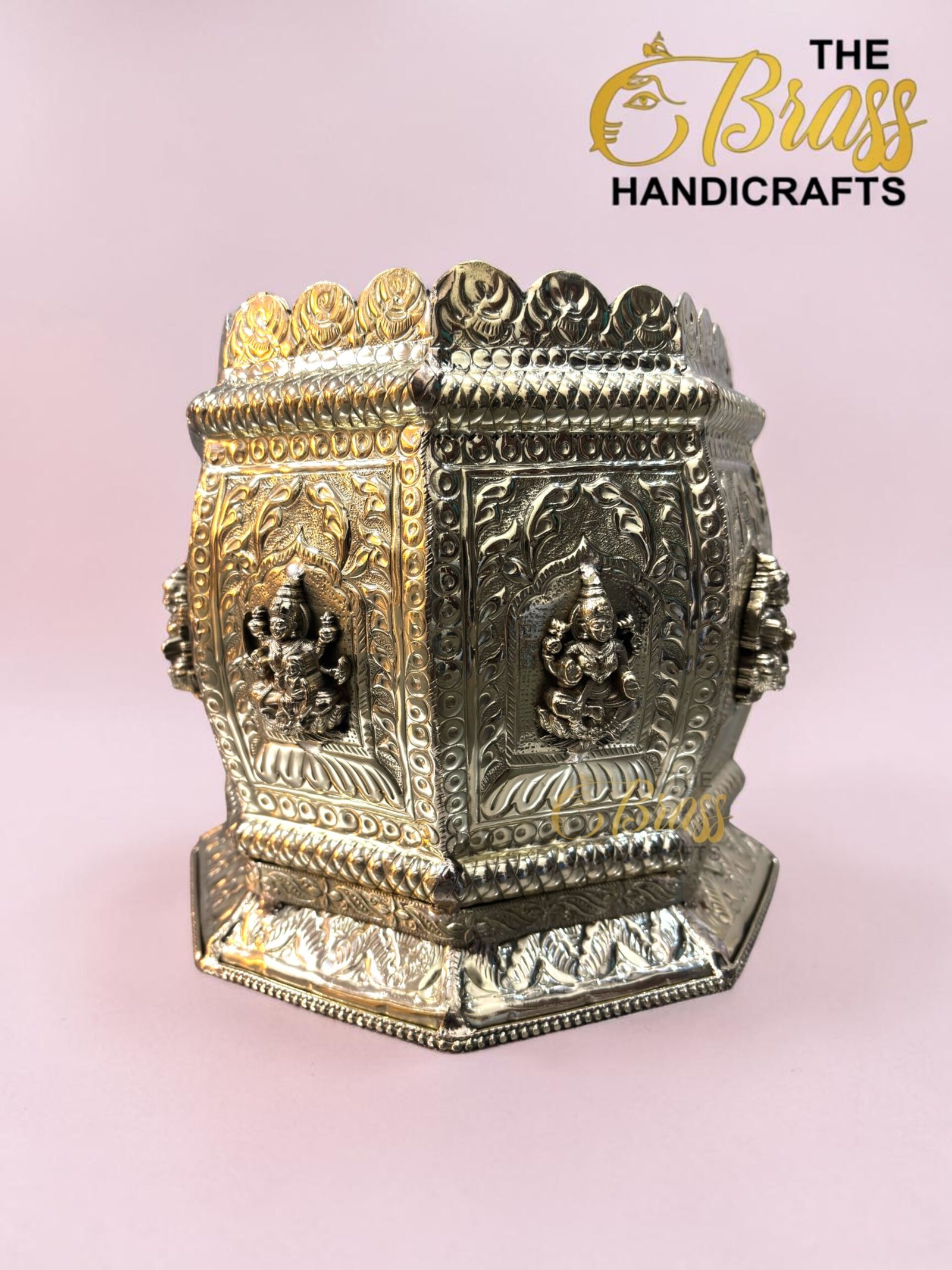 Ornate silver metal decorative shrine with embossed panels and small figurines, set against a pink background.  thebrasshandicrafts.com