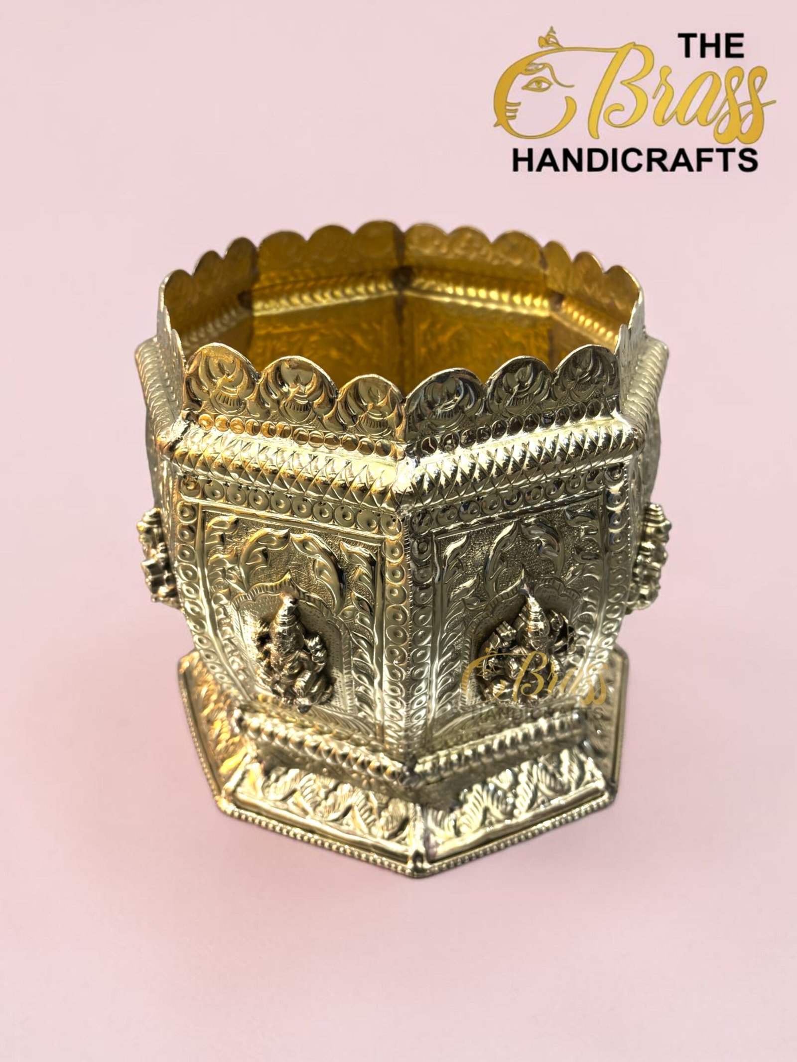 Ornate gold-toned metal decorative crown-like vessel with embossed patterns on a pink backdrop  thebrasshandicrafts.com