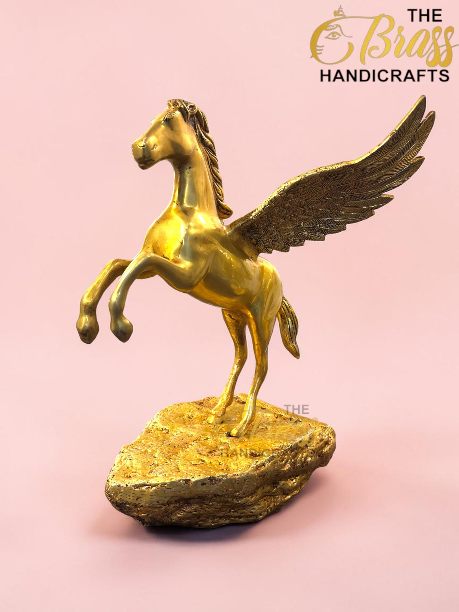 Golden Pegasus statue with wings raised, standing on a rocky base against a pink background.  thebrasshandicrafts.com