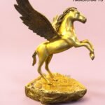 Golden Pegasus statue with wings extended on a textured pedestal, pink background and The Brass Handicrafts logo in the corner.  thebrasshandicrafts.com