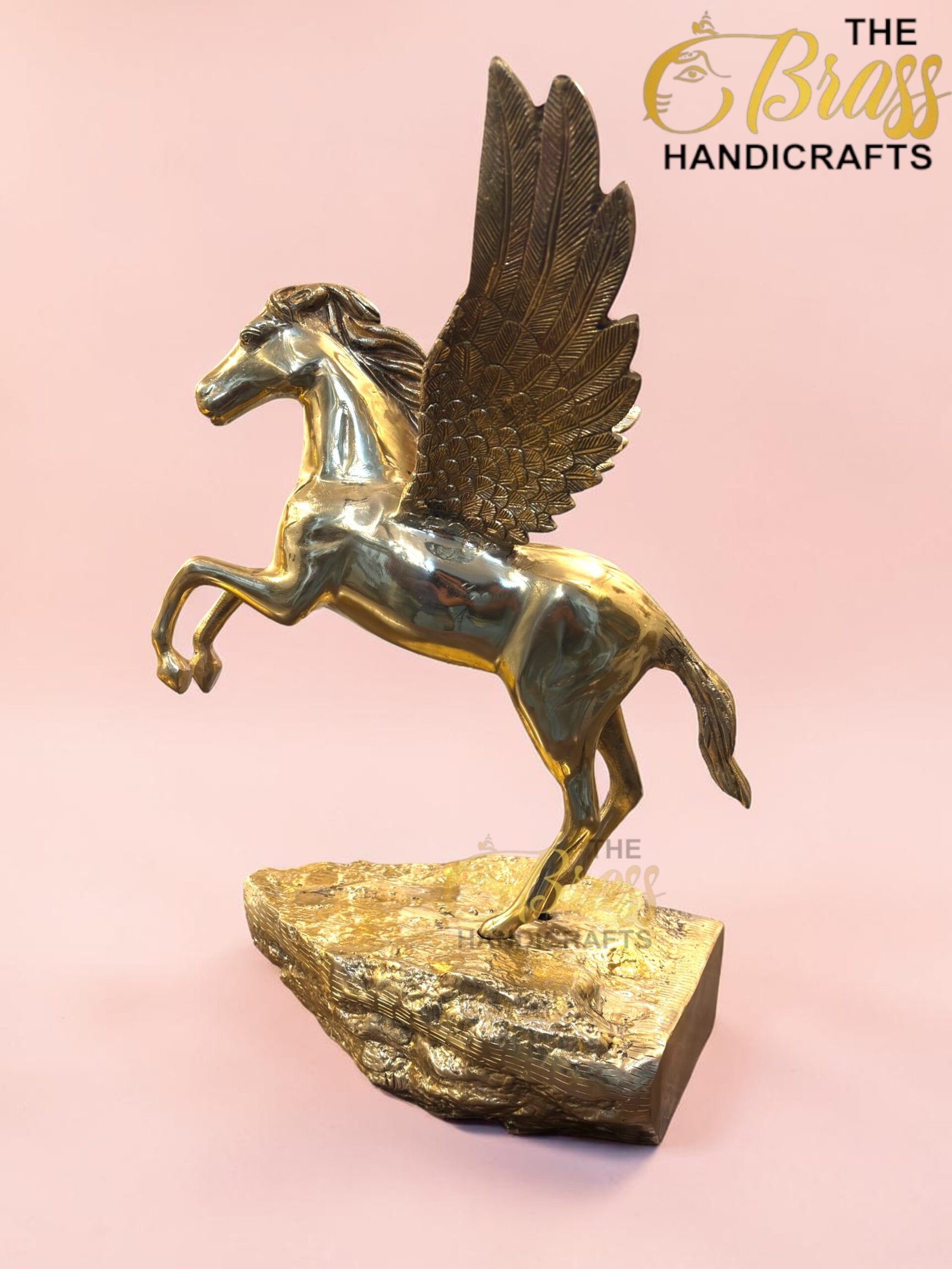 Gold-toned Pegasus statue with spread wings perched on a textured rock base against a pink background, a brass handicraft.  thebrasshandicrafts.com