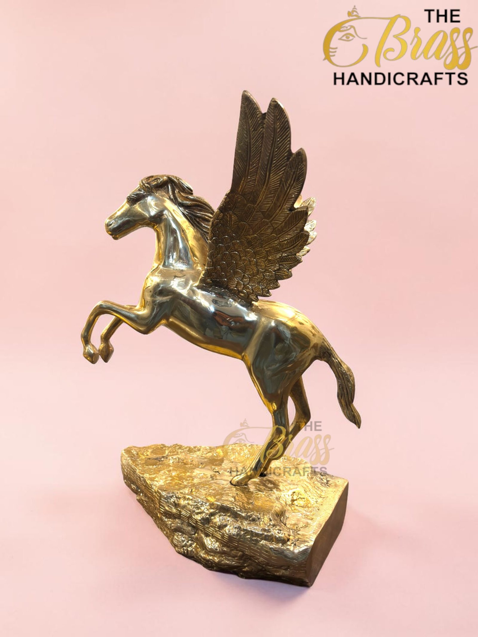 Brass gold-toned statue of a winged horse (Pegasus) rearing on a rocky base against a pink backdrop.  thebrasshandicrafts.com