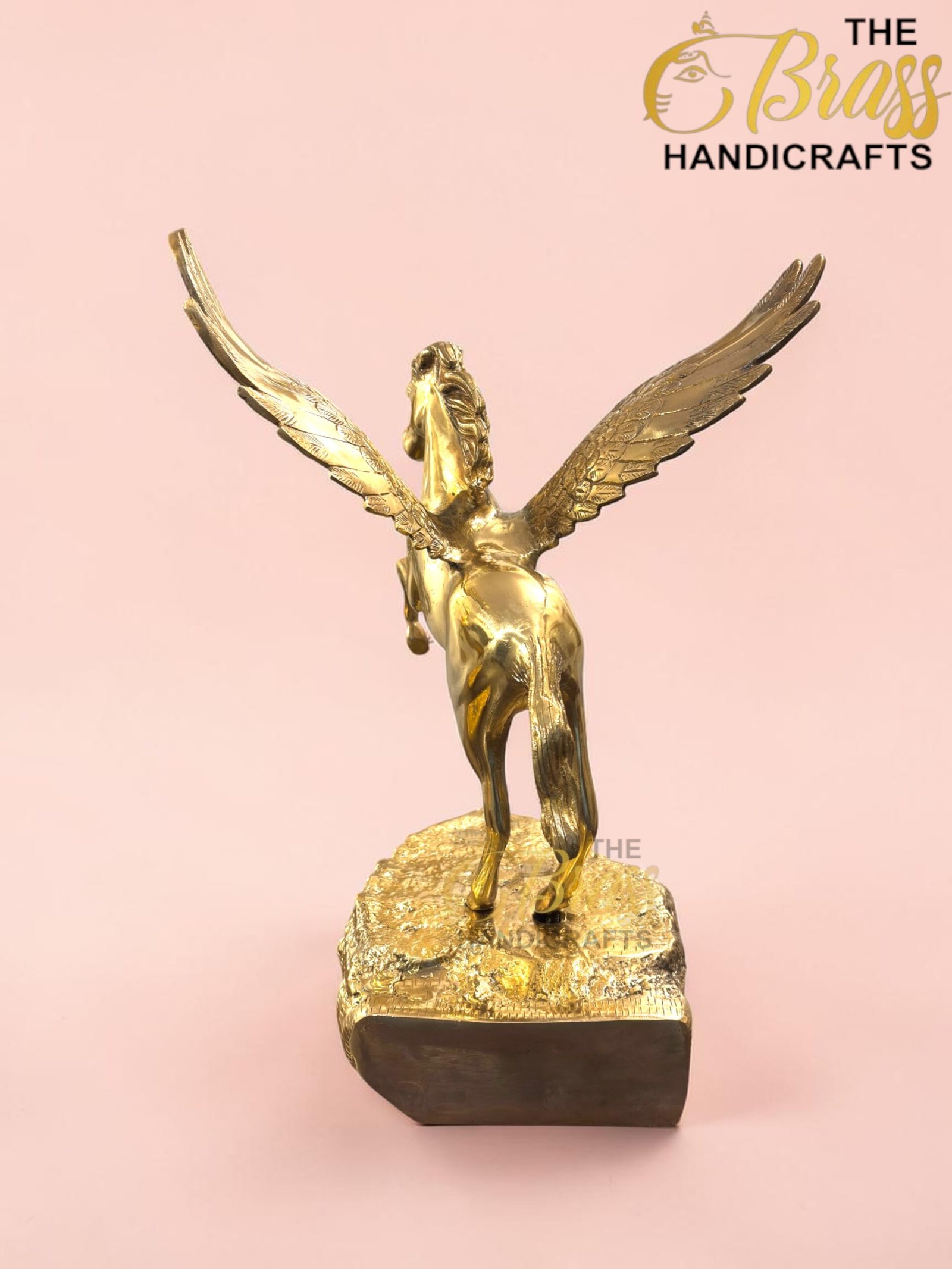 Gold statue of a winged horse (Pegasus) rearing on a textured pedestal against a pink background with a subtle logo watermark nearby.  thebrasshandicrafts.com
