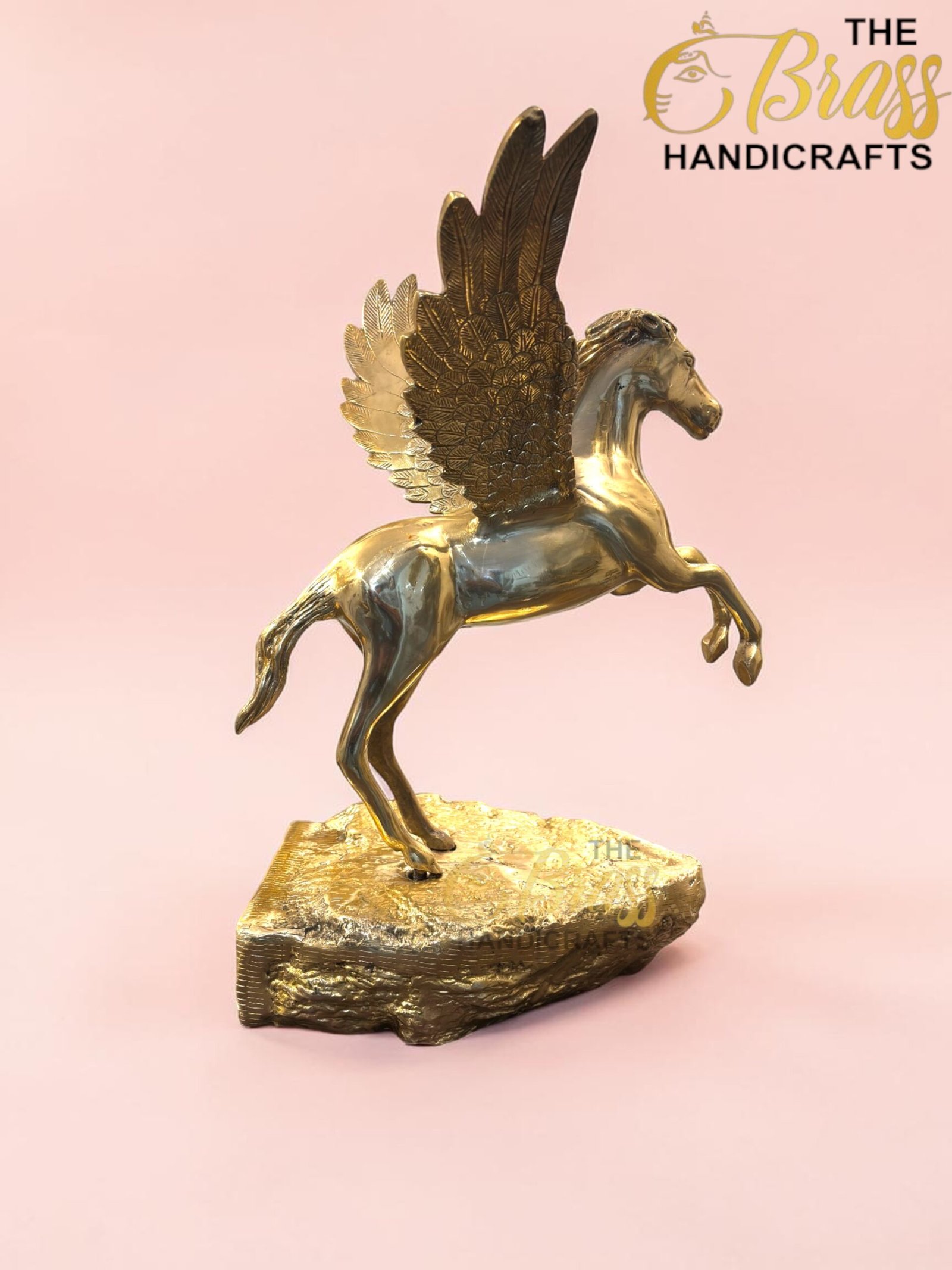 Golden Pegasus sculpture with spread wings perched on a rocky base against a pink background.  thebrasshandicrafts.com