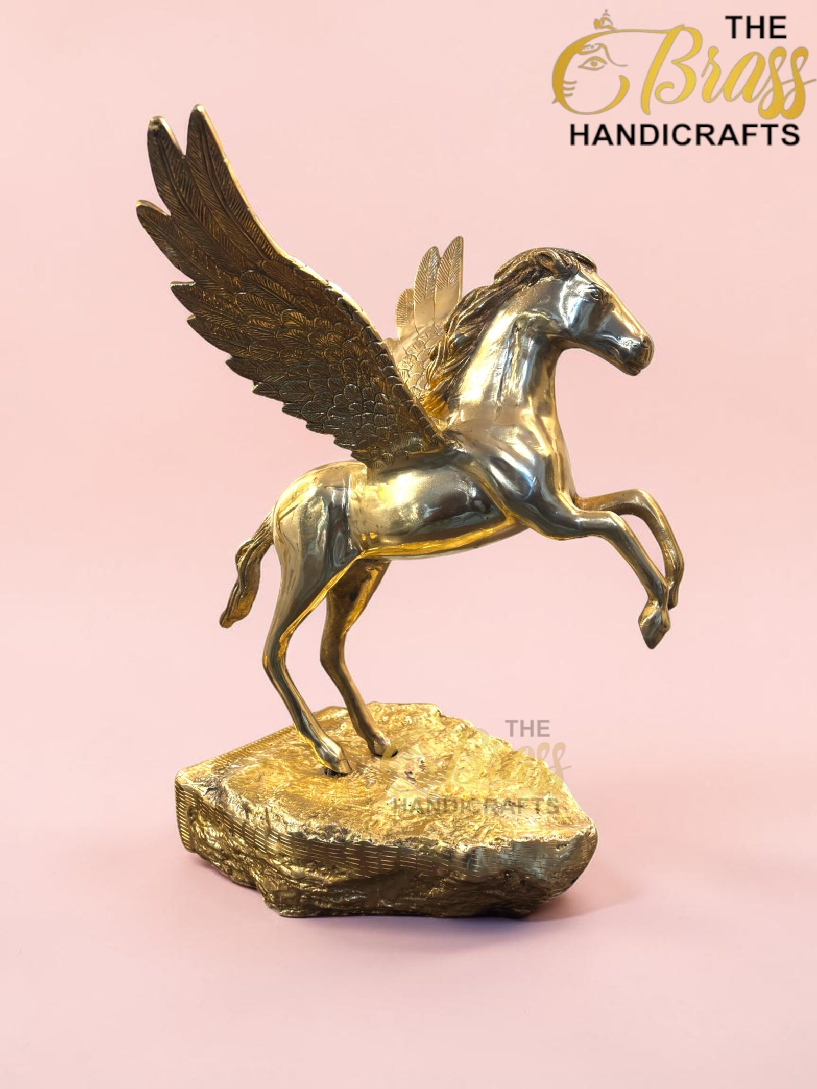 Gold Pegasus sculpture with wings spread, standing on a textured pedestal against a pink background; features 'The Brass Handicrafts' logo in the corner.  thebrasshandicrafts.com
