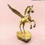 Gold Pegasus sculpture with wings spread, rearing on a textured square base against a pale pink background, product photo.  thebrasshandicrafts.com