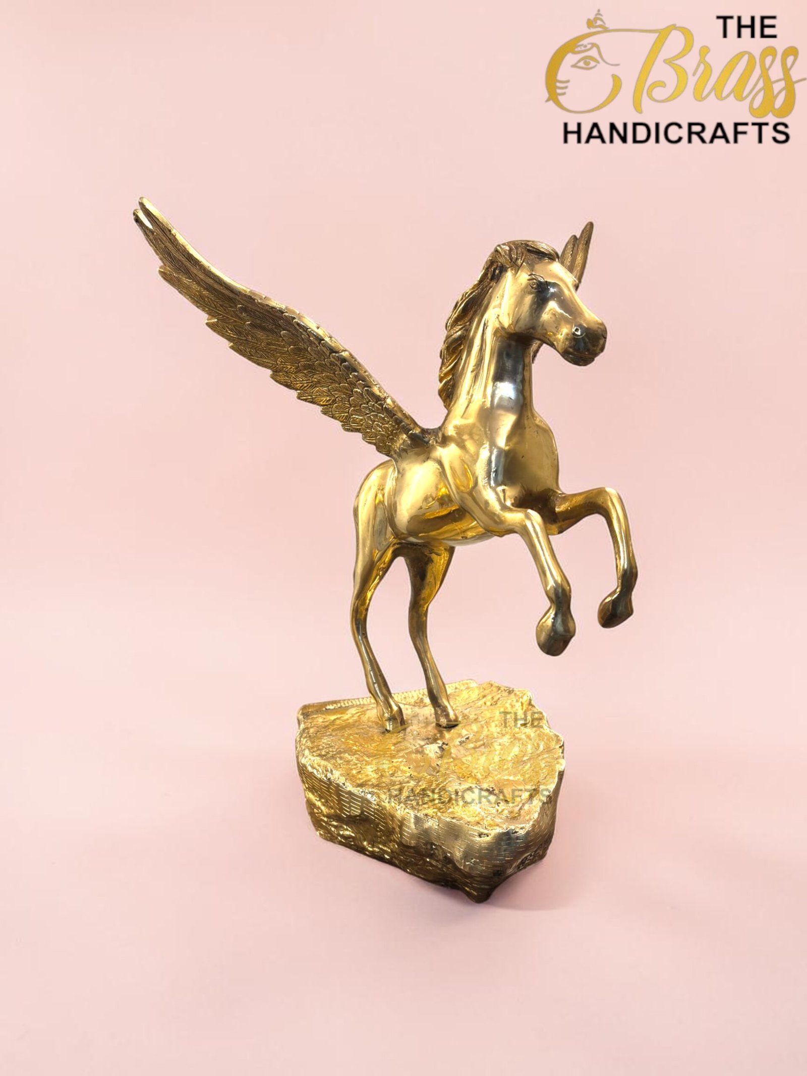 Gold Pegasus sculpture with wings spread, rearing on a textured square base against a pale pink background, product photo.  thebrasshandicrafts.com