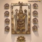 Ornate gold metal Hindu idol framed by a large decorative gold frame, with smaller arched plaques on each side, displayed on a beige wall with a 'Brass Handicrafts' watermark.  thebrasshandicrafts.com