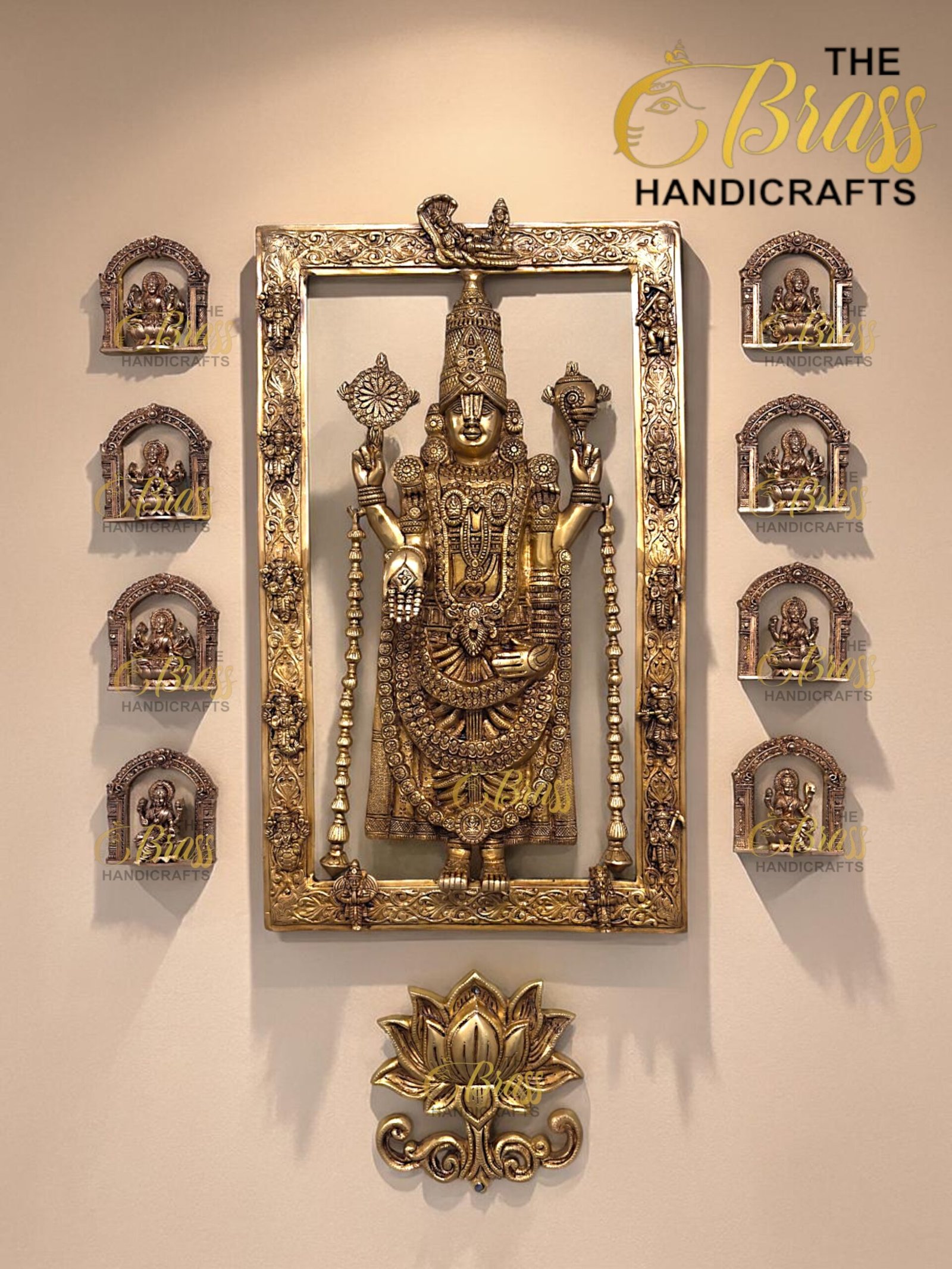 Ornate gold metal Hindu idol framed by a large decorative gold frame, with smaller arched plaques on each side, displayed on a beige wall with a 'Brass Handicrafts' watermark.  thebrasshandicrafts.com