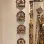 Metal decorative Hindu deities in ornate arched niches mounted on a beige wall, with a tall gold ornamental frame to the right  thebrasshandicrafts.com