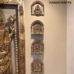 Gold-toned Hindu deity statue in an ornate frame, with smaller intricate brass figures mounted on a beige wall.  thebrasshandicrafts.com