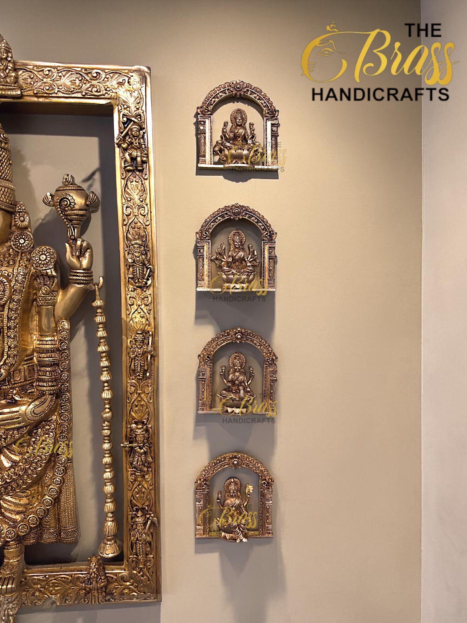 Gold-toned Hindu deity statue in an ornate frame, with smaller intricate brass figures mounted on a beige wall.  thebrasshandicrafts.com