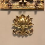Close-up of a gold-toned decorative brass panel with intricate floral scrollwork and a lotus flower ornament at the bottom, used as wall art  thebrasshandicrafts.com