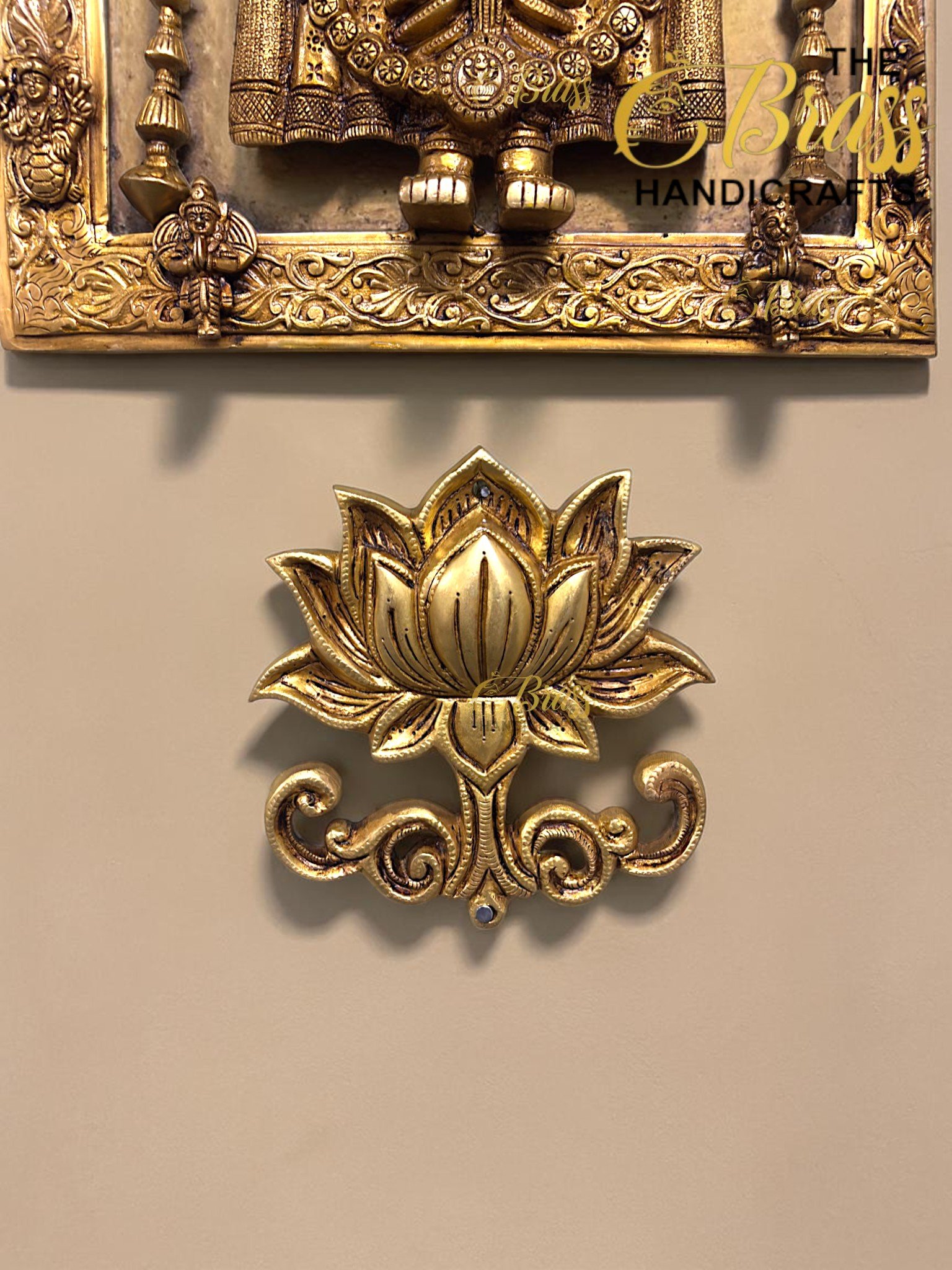 Close-up of a gold-toned decorative brass panel with intricate floral scrollwork and a lotus flower ornament at the bottom, used as wall art  thebrasshandicrafts.com