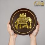 Person holding a round wooden shield with a gold embossed elephant design; brand logo in the top-right corner reads 'The Boss Handicrafts'.  thebrasshandicrafts.com