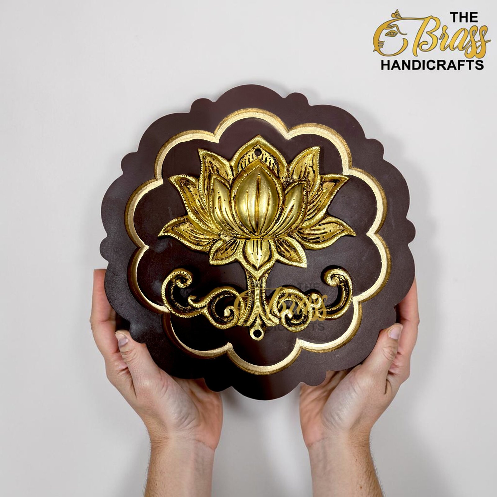 Ornate brown decorative plaque with gold floral design, held by two hands in front of a light background.  thebrasshandicrafts.com