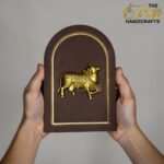 Hands hold a brown arch-shaped plaque with a gold embossed horse relief and a gold border against a gray background.  thebrasshandicrafts.com