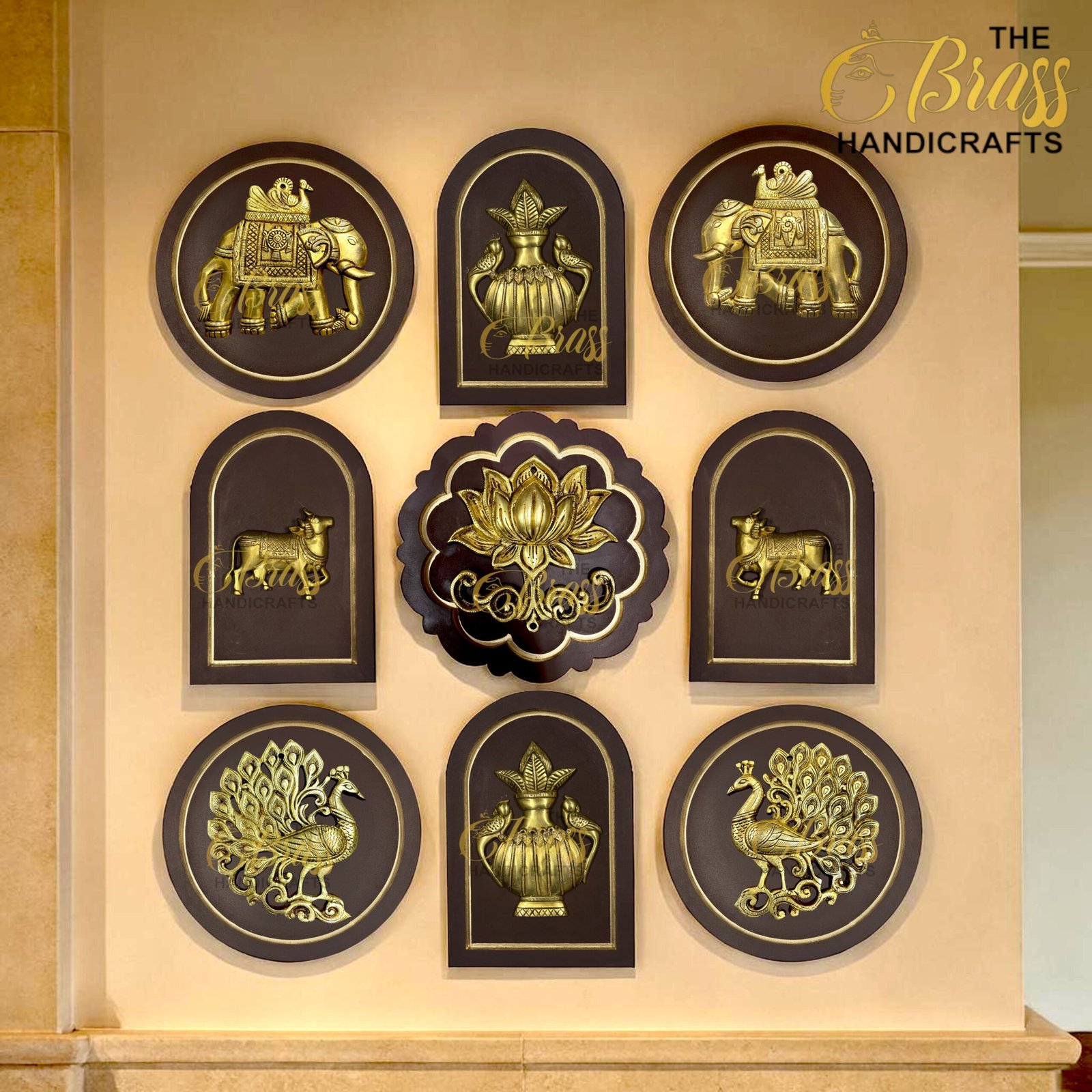 Row of gold embossed handicraft plaques on dark frames featuring elephant, vase, peacock and floral motifs at display wall  thebrasshandicrafts.com