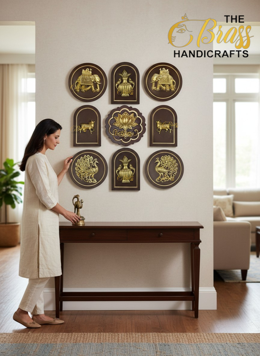 Woman in a light outfit stands by a dark wooden console table, admiring a wall display of gold brass plaques in circular, arched, and floral shapes  thebrasshandicrafts.com