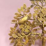Gold decorative brass tree sculpture with leaves and a bird, set against a pink background, branding reads 'The Brass Handicrafts' (decorative product image).  thebrasshandicrafts.com