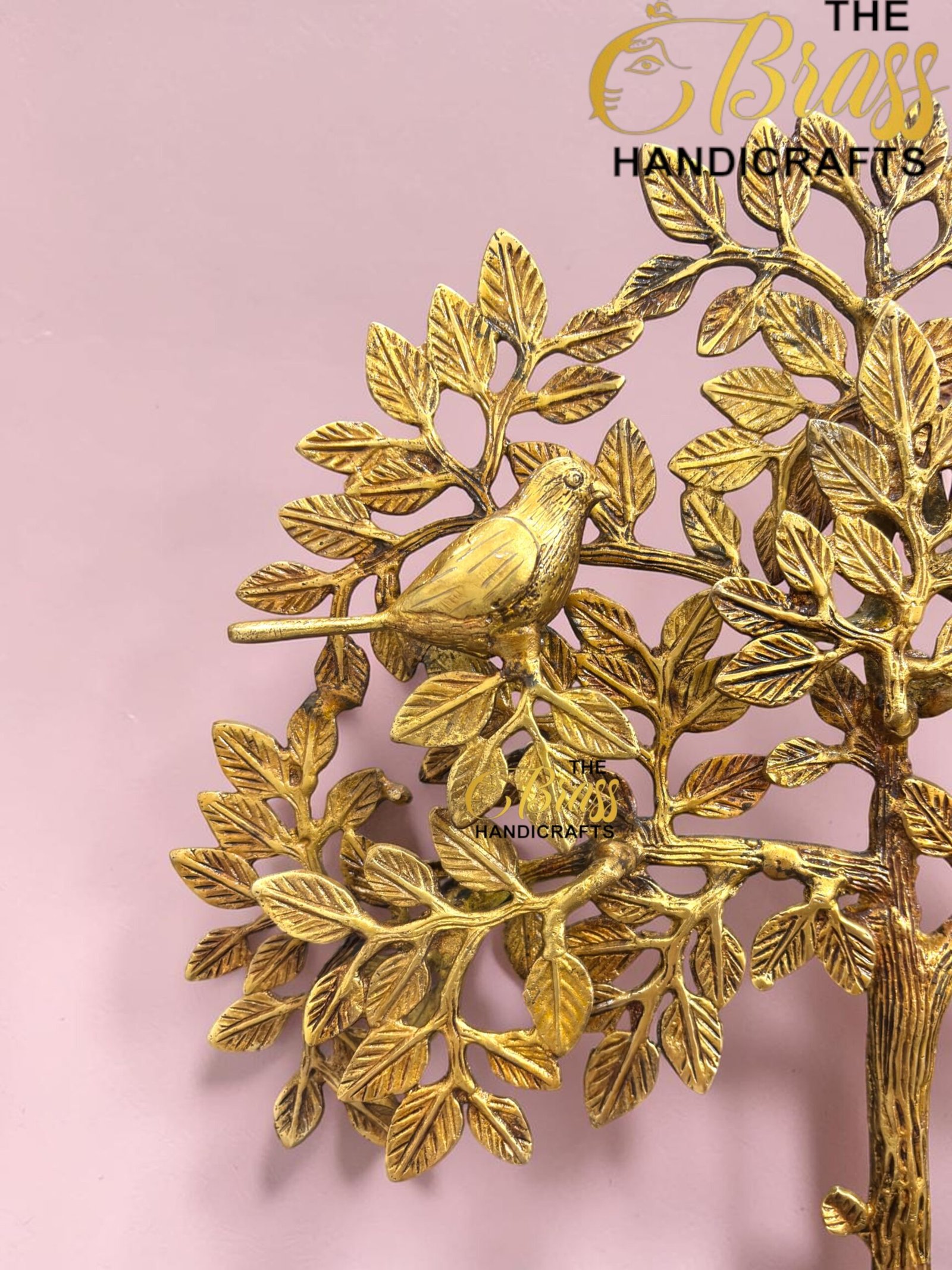 Gold decorative brass tree sculpture with leaves and a bird, set against a pink background, branding reads 'The Brass Handicrafts' (decorative product image).  thebrasshandicrafts.com