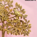 Gold metal tree sculpture with detailed leaves on a pink background, featuring a partial logo reading 'The Brass Handicrafts' in the upper right.  thebrasshandicrafts.com