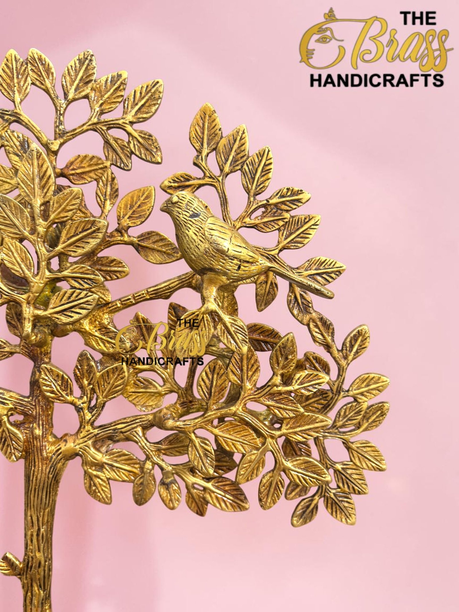 Gold metal tree sculpture with detailed leaves on a pink background, featuring a partial logo reading 'The Brass Handicrafts' in the upper right.  thebrasshandicrafts.com
