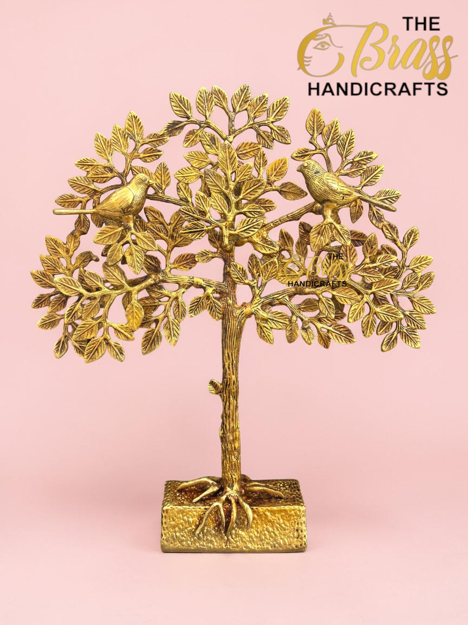 Gold metal tree sculpture with two birds perched on branching limbs against a pink backdrop, branded 'The Brass Handicrafts' in the corner  thebrasshandicrafts.com
