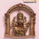 Ornate gold brass statue of a Hindu deity inside an intricate arch frame on a pink background, with 'The Brass Handicrafts' logo in the corner.  thebrasshandicrafts.com