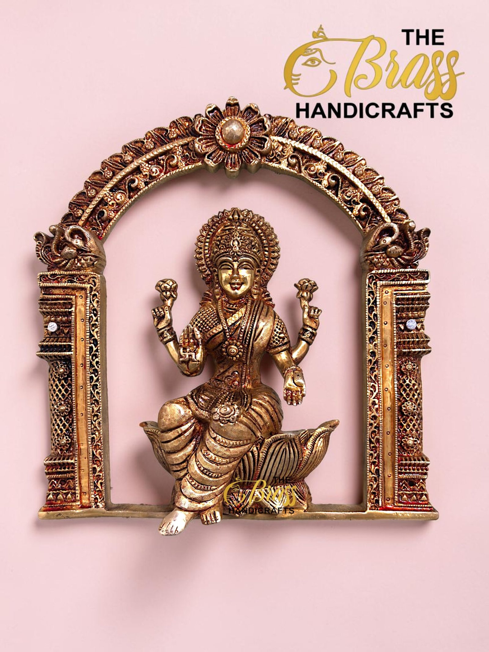 Gold-toned Hindu goddess statue set in an ornate carved arch on a pink background (The Brass Handicrafts).  thebrasshandicrafts.com