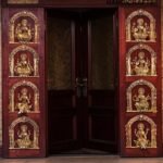 Wooden doors with gold Brahma-like deity panels set in carved arches on both sides of the doorway.  thebrasshandicrafts.com