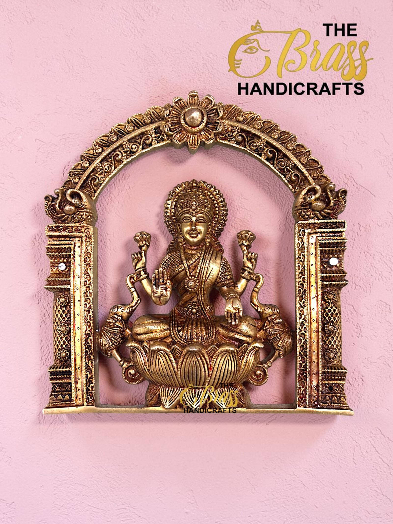 Ornate gold statue of a deity seated in a decorative arch frame on a pink wall, with 'The Boss Handicrafts' logo in the corner.  thebrasshandicrafts.com