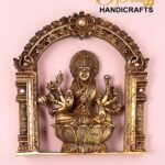 Gold brass statue of a multi-armed Hindu deity seated on a lotus, within an ornate arch against a pink background.  thebrasshandicrafts.com