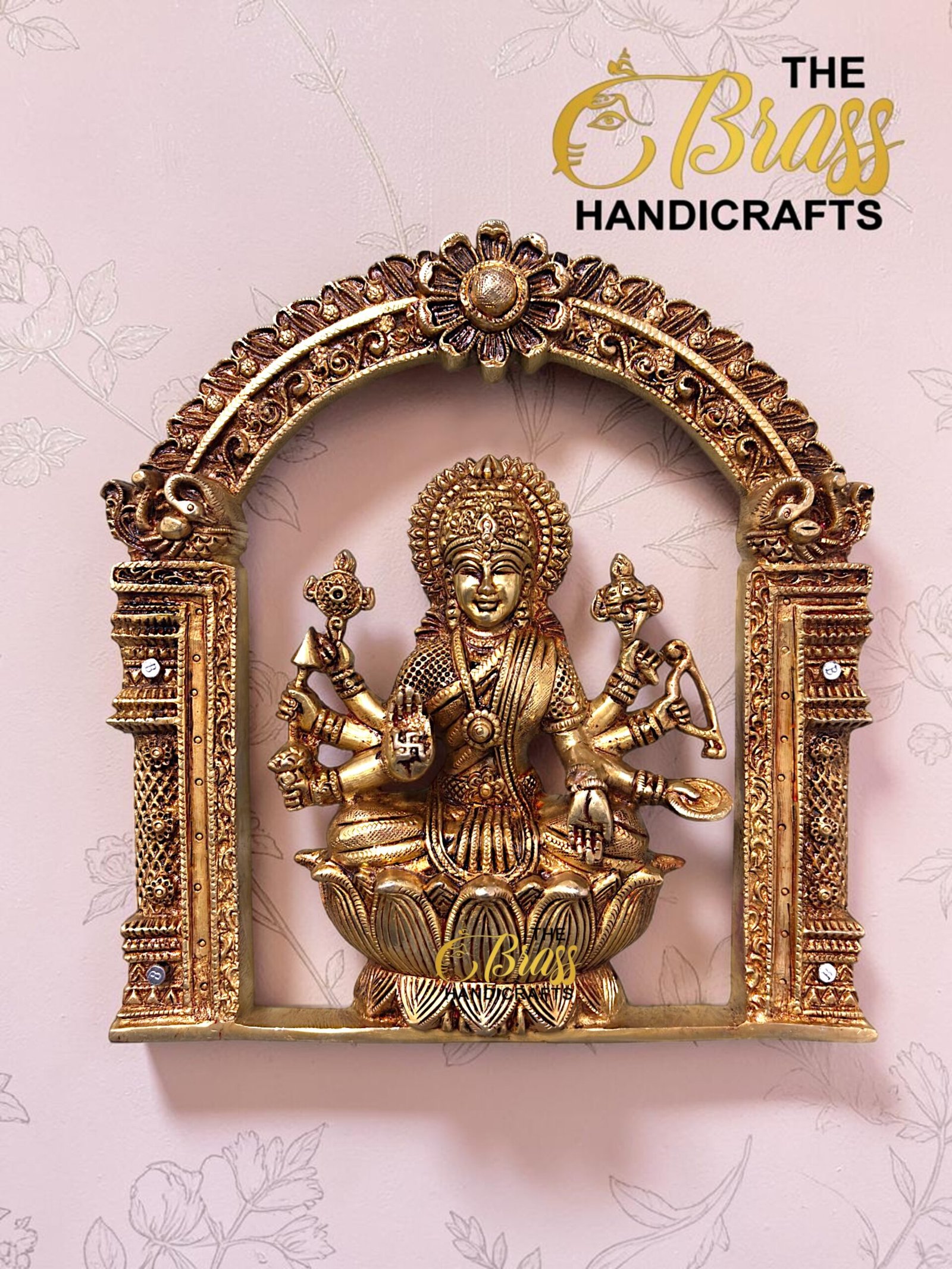 Gold-toned Lakshmi statue seated on a lotus, inside an ornate arch, with 'The Bliss Handicrafts' logo in the top right.  thebrasshandicrafts.com