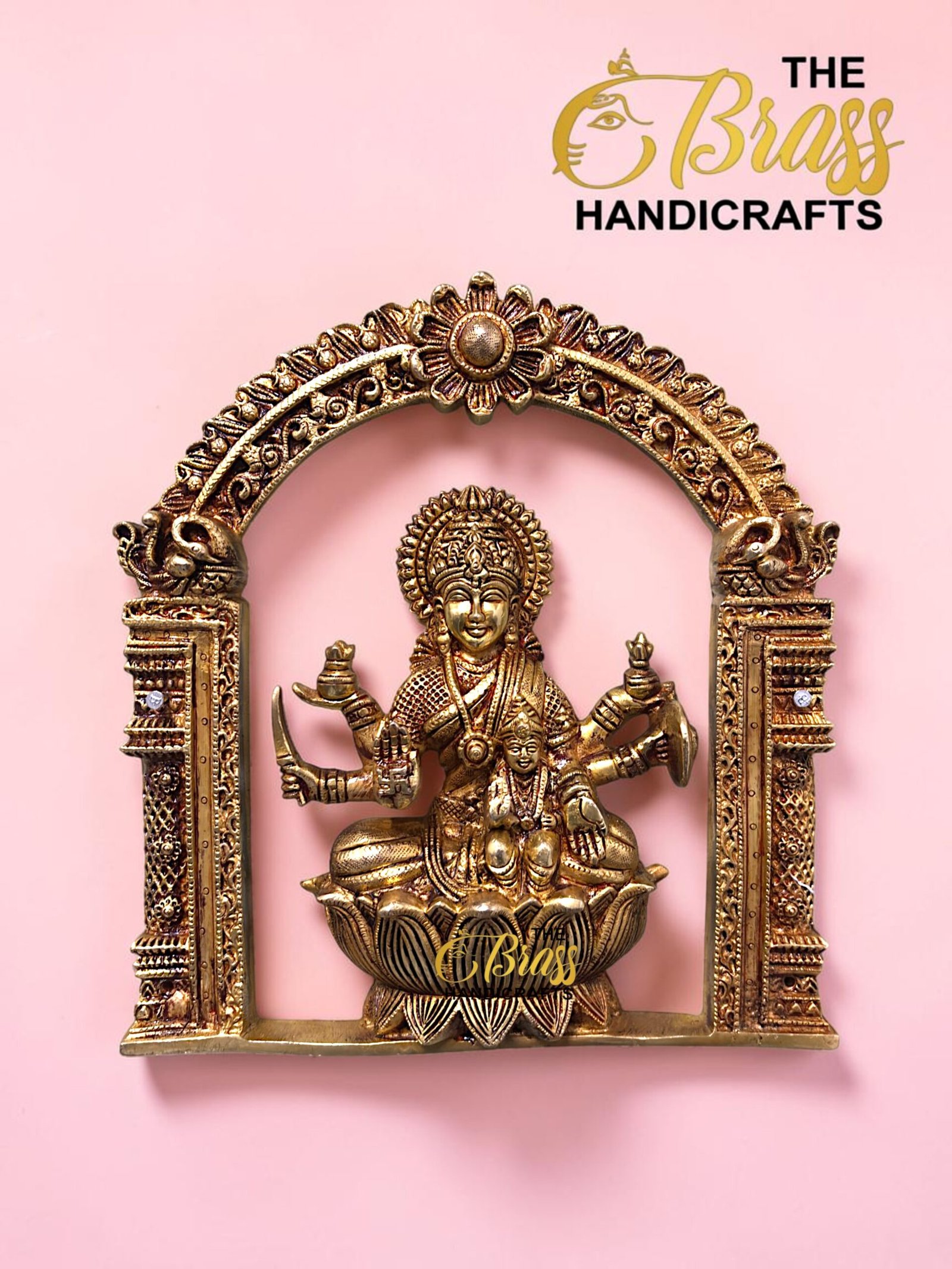Ornate gold brass statue framed by a carved arch, set against a pink background; logo reads The Brass Handicrafts in the corner.  thebrasshandicrafts.com