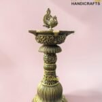 Ornate brass lamp base with a swan finial and intricate floral patterns against a pale pink background.  thebrasshandicrafts.com
