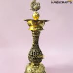 Intricately carved brass decorative piece with an ornate bird finial atop, set against a pink background. (Brand: The Brass Handicrafts)  thebrasshandicrafts.com