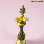 Decorative, ornate brass hookah with a detailed top finial against a pink background.  thebrasshandicrafts.com