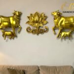 Golden wall sculpture: two golden cows on either side of a central ornate lotus motif, mounted above a beige sofa.  thebrasshandicrafts.com