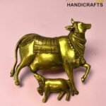 Gold brass statue of a decorated cow with saddle and beaded necklace on a pink background.  thebrasshandicrafts.com