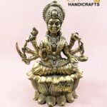 IMG_5775 - thebrasshandicrafts.com Brass statue of a multi-armed Hindu goddess seated on a lotus, against a pale pink background, with 'The Brass Handicrafts' logo nearby. thebrasshandicrafts.com