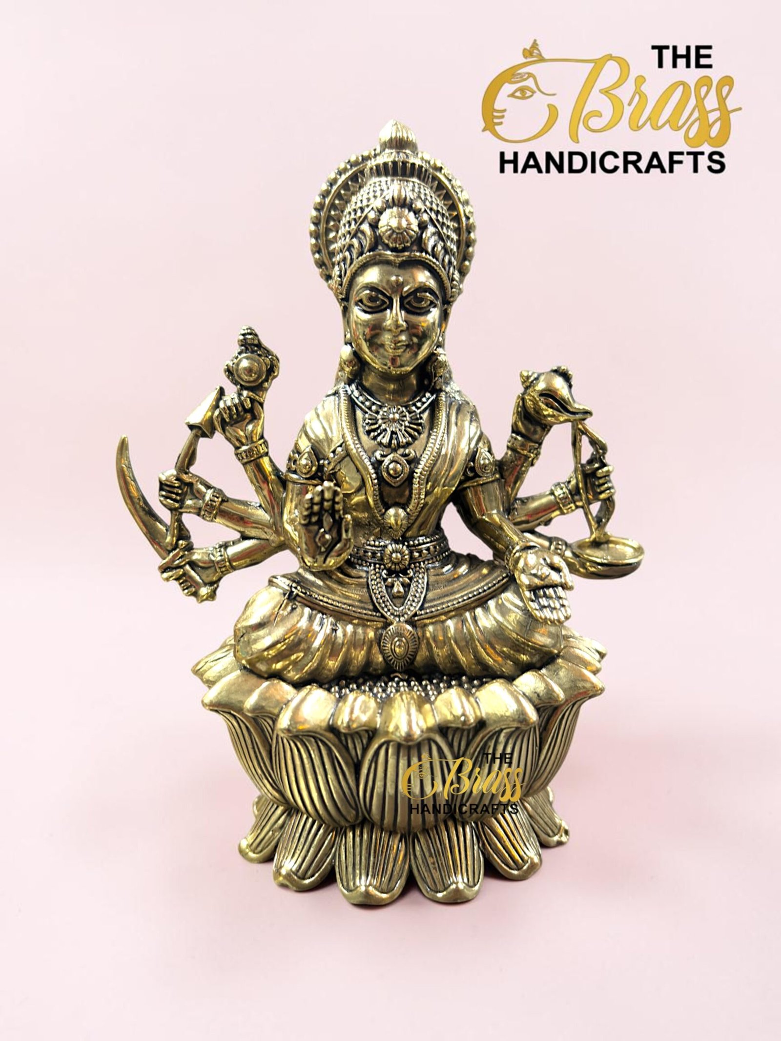IMG_5775 - thebrasshandicrafts.com Brass statue of a multi-armed Hindu goddess seated on a lotus, against a pale pink background, with 'The Brass Handicrafts' logo nearby. thebrasshandicrafts.com